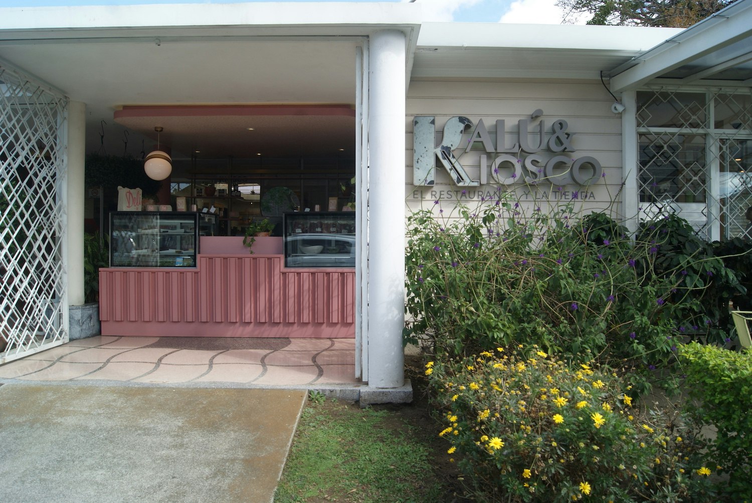 Exterior shot of Kalú restaurant. Just beyond the door frame is a bright pink counter with glass containers on opposite sides.